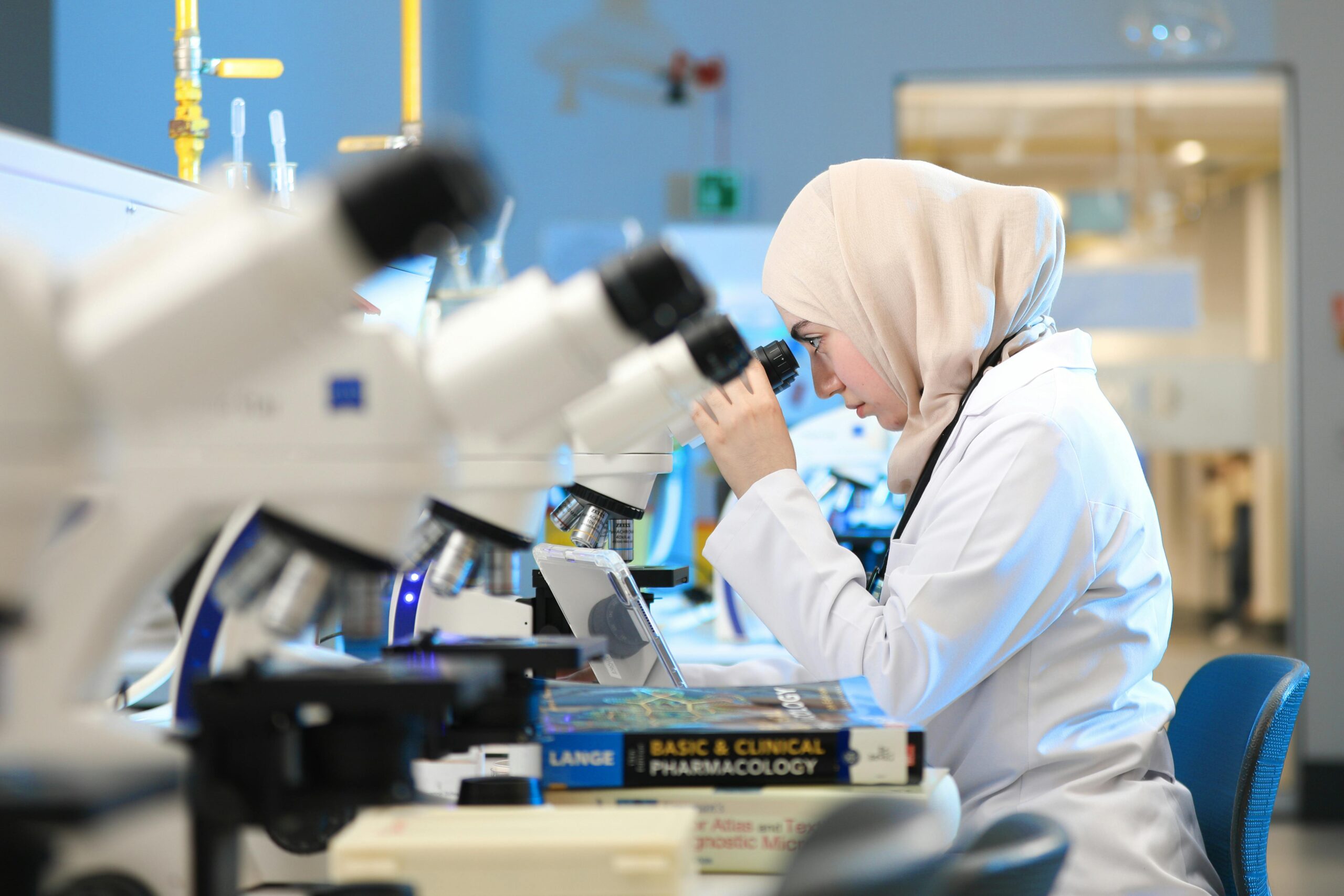 A scientist in a lab coat examines samples through a microscope in a modern laboratory setting.