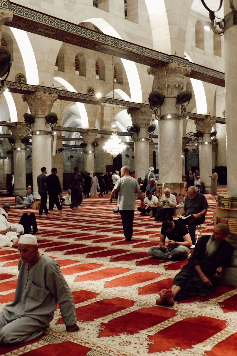 People gathered in a grand mosque interior, sitting and praying in a peaceful ambiance.