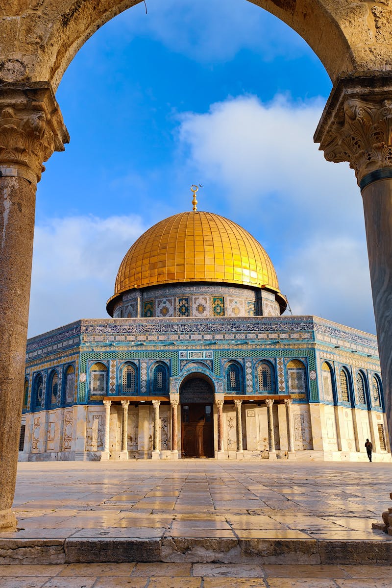 Stunning view of the Dome of the Rock with its golden dome through an ancient archway, showcasing Islamic architecture.