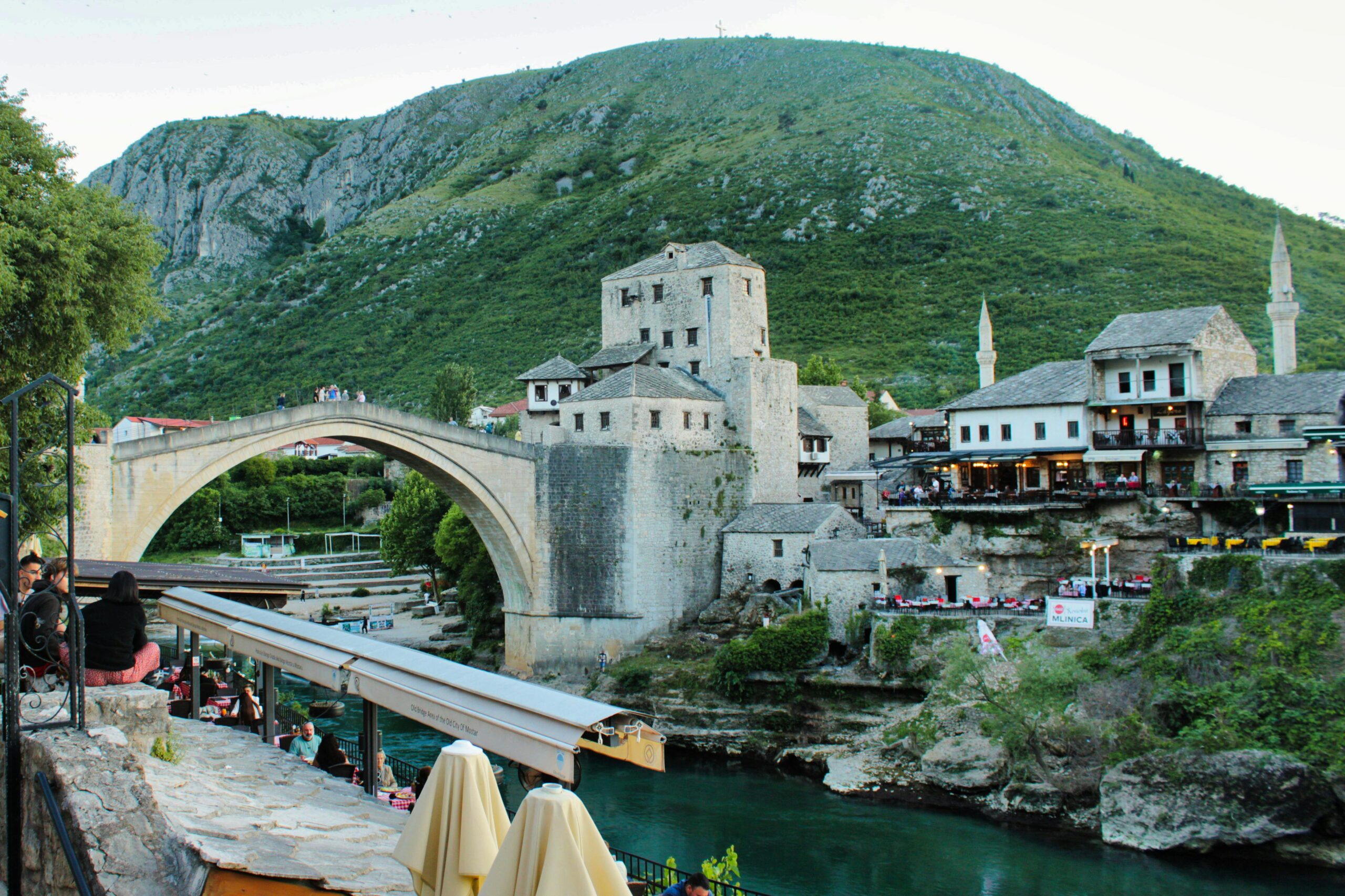 Explore the historic Old Bridge in Mostar, surrounded by lush hills and vibrant architecture.
