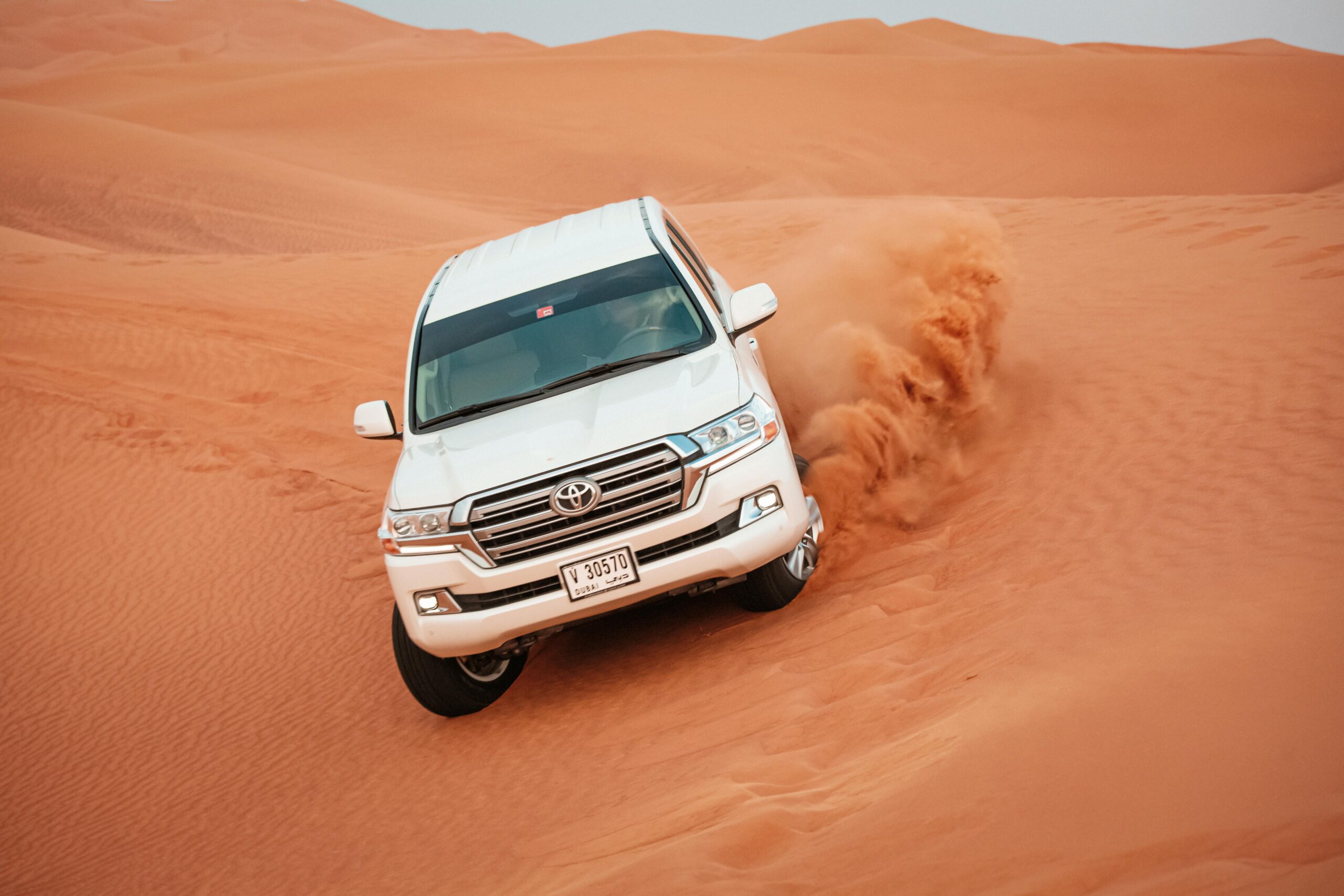 A Toyota Land Cruiser navigating a challenging desert dune, showcasing off-road capabilities.