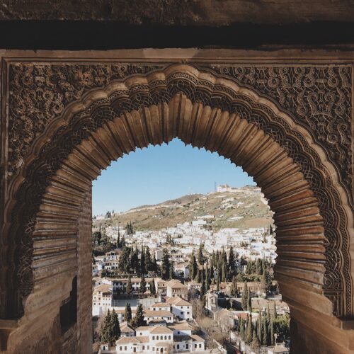 A beautifully ornamented archway in the Alhambra frames a picturesque view of Granada, Spain.