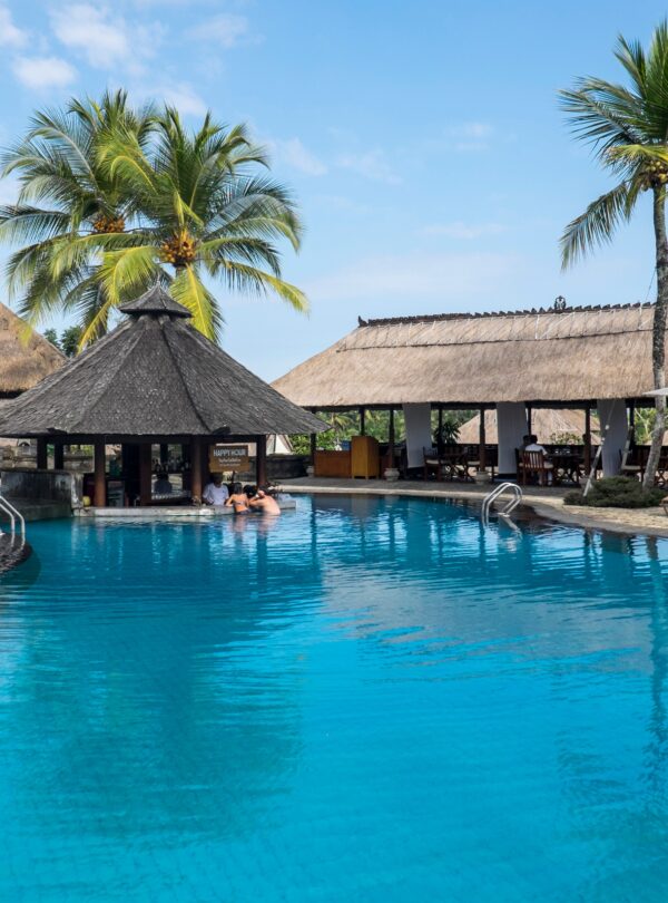 Relax by the tropical pool at a luxurious resort in Bali, featuring palm trees and serene blue waters.