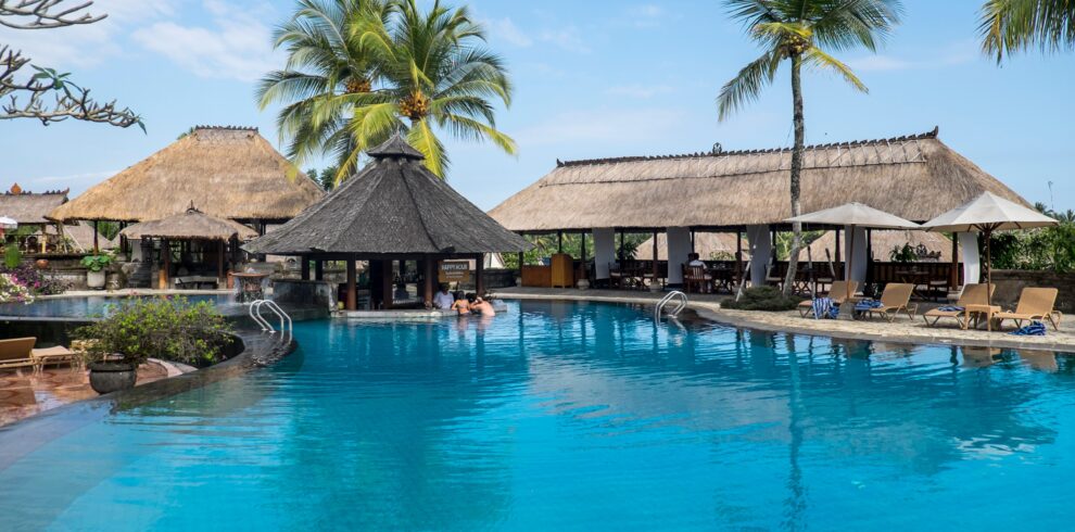 Relax by the tropical pool at a luxurious resort in Bali, featuring palm trees and serene blue waters.