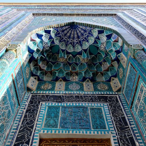 Close-up of intricate blue and turquoise Islamic tiles on a building facade.
