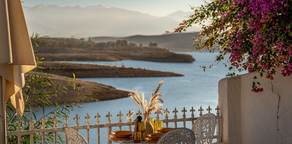 Charming outdoor dining scene with colorful flowers and serene lake view at sunset.